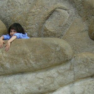Little girl in the hand of a big stone statue