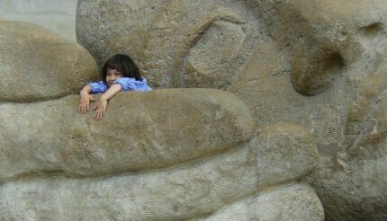 Little girl in the hand of a big stone statue